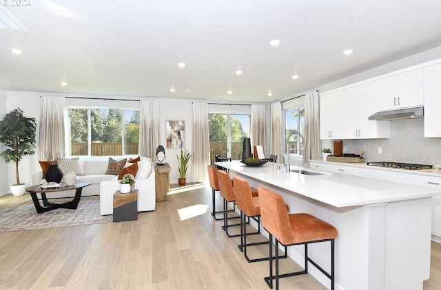 kitchen featuring stainless steel gas stovetop, a healthy amount of sunlight, white cabinetry, and a large island with sink