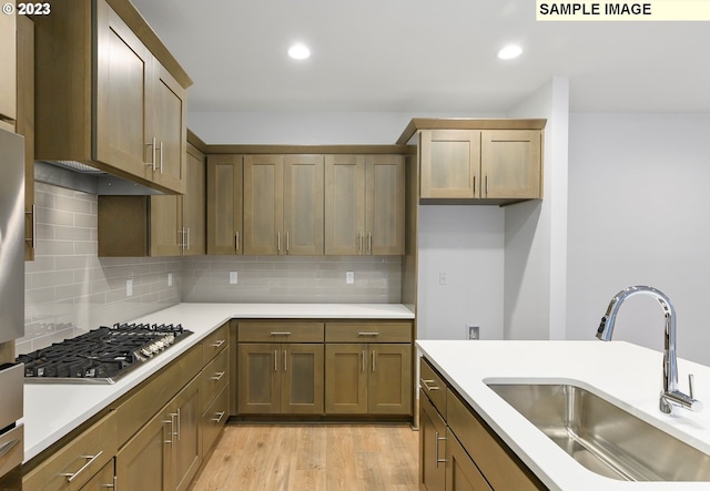 kitchen featuring stainless steel gas stovetop, light hardwood / wood-style floors, backsplash, and sink