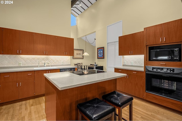 kitchen with hanging light fixtures, black appliances, a breakfast bar, high vaulted ceiling, and light hardwood / wood-style floors