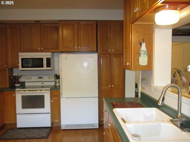 kitchen with white appliances, wood-type flooring, and sink