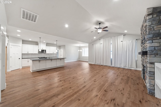 unfurnished living room featuring ceiling fan, sink, light hardwood / wood-style floors, a stone fireplace, and lofted ceiling