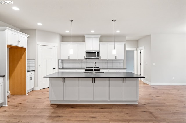 kitchen with light wood-type flooring, sink, decorative light fixtures, and an island with sink