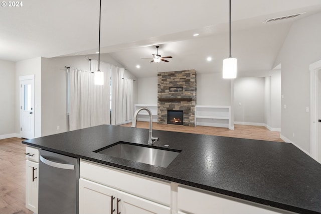 kitchen featuring sink, a stone fireplace, lofted ceiling, white cabinets, and light wood-type flooring