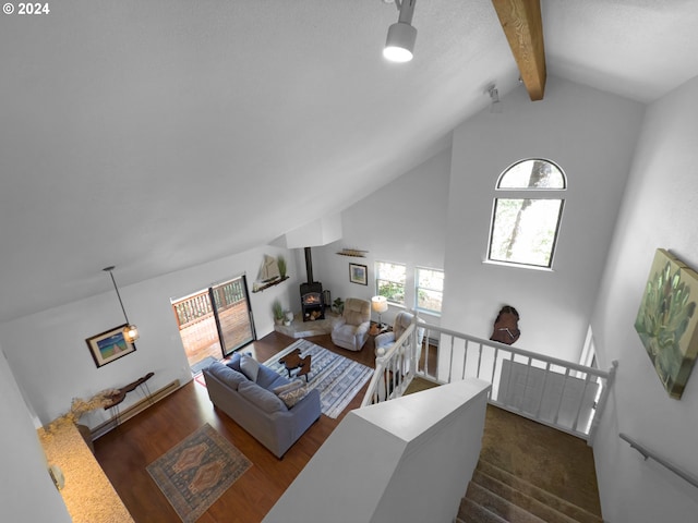 living room featuring beam ceiling, a wood stove, high vaulted ceiling, and dark carpet