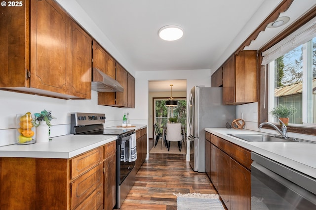 kitchen featuring brown cabinets, under cabinet range hood, a sink, appliances with stainless steel finishes, and light countertops