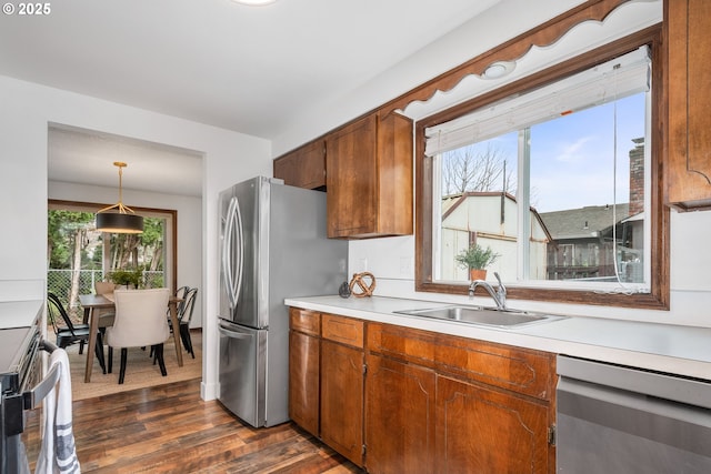 kitchen featuring dark wood finished floors, light countertops, hanging light fixtures, stainless steel appliances, and a sink