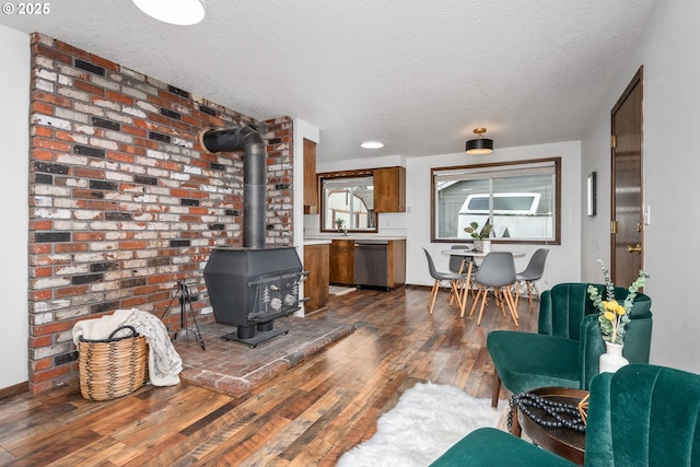 living area featuring a textured ceiling, dark wood-style floors, brick wall, baseboards, and a wood stove