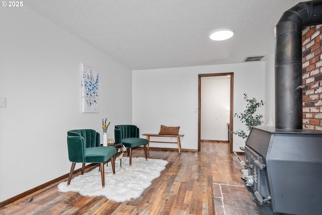 sitting room featuring visible vents, a textured ceiling, a wood stove, and hardwood / wood-style flooring