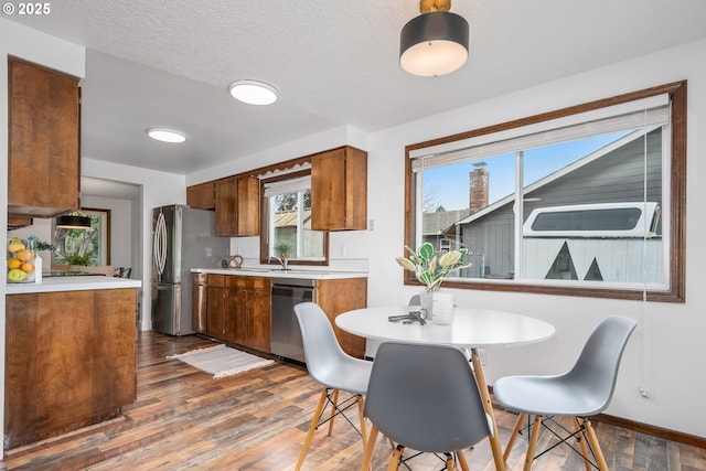 kitchen featuring brown cabinets, a textured ceiling, dark wood-style floors, appliances with stainless steel finishes, and light countertops