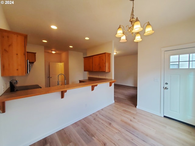 kitchen featuring kitchen peninsula, stove, light hardwood / wood-style floors, decorative light fixtures, and a breakfast bar