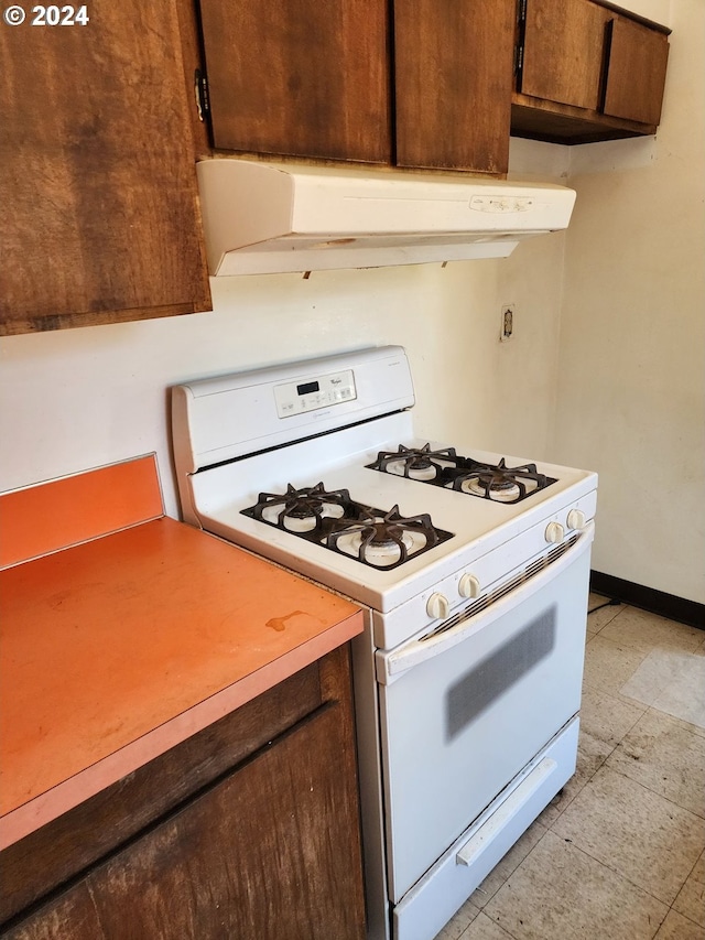 kitchen featuring white gas stove, wall chimney exhaust hood, and light tile flooring