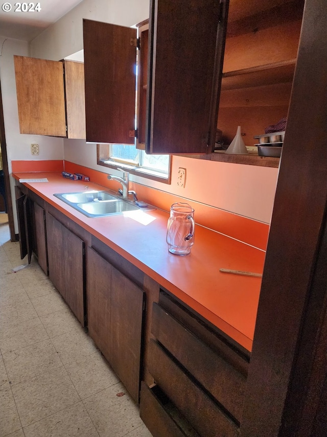 kitchen with dark brown cabinetry, sink, and light tile floors