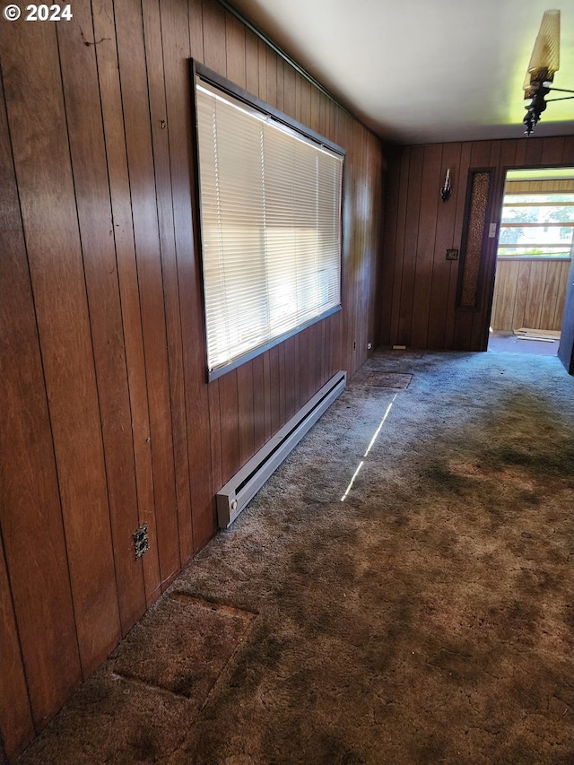 hall featuring wood walls, baseboard heating, and carpet flooring