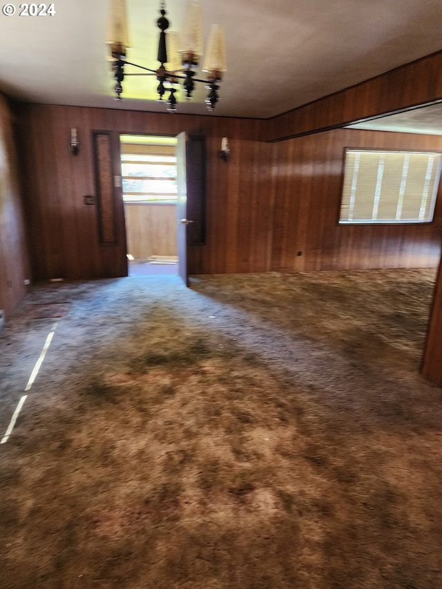 unfurnished room with a notable chandelier, wood walls, and carpet flooring