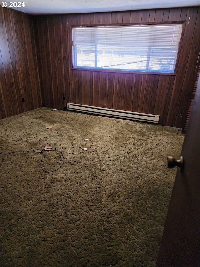 carpeted spare room featuring wooden walls and a baseboard heating unit