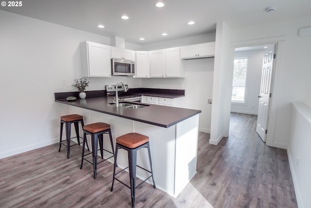 kitchen with a peninsula, dark countertops, white cabinetry, and appliances with stainless steel finishes