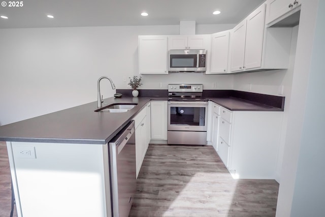 kitchen featuring dark countertops, appliances with stainless steel finishes, white cabinets, a sink, and a peninsula