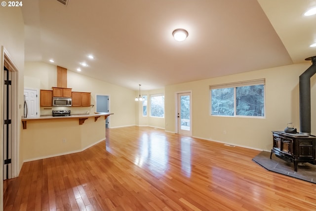 living room featuring a wood stove, light hardwood / wood-style floors, lofted ceiling, and an inviting chandelier