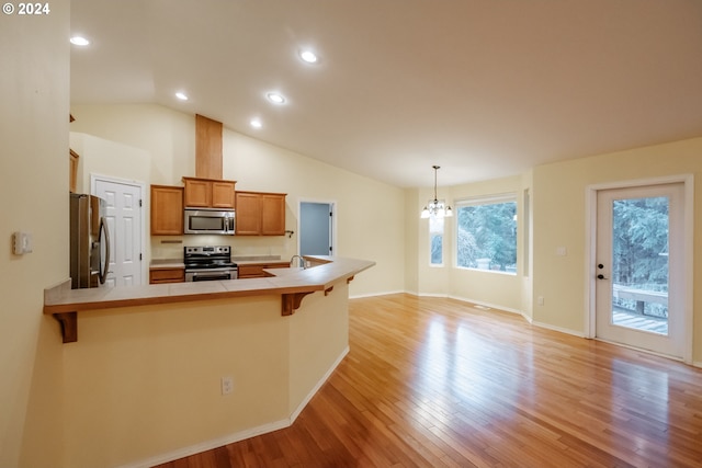 kitchen featuring hanging light fixtures, a breakfast bar area, light wood-type flooring, kitchen peninsula, and stainless steel appliances