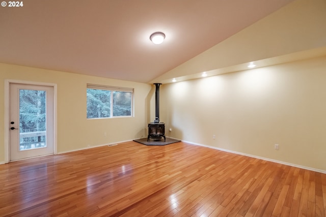 unfurnished living room with a wood stove, lofted ceiling, and light wood-type flooring