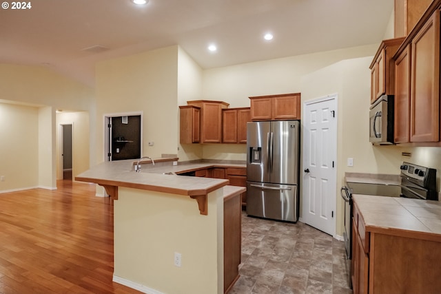 kitchen with kitchen peninsula, tile countertops, stainless steel fridge with ice dispenser, black range with electric stovetop, and a breakfast bar area