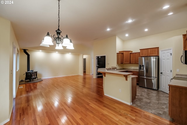 kitchen with a wood stove, an inviting chandelier, stainless steel refrigerator with ice dispenser, decorative light fixtures, and a breakfast bar