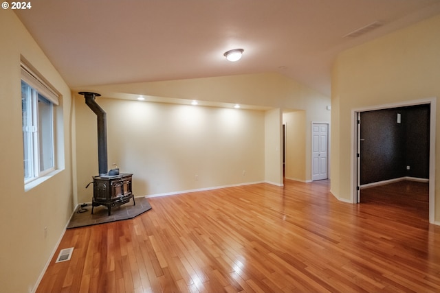 unfurnished living room featuring a wood stove, light hardwood / wood-style flooring, and vaulted ceiling