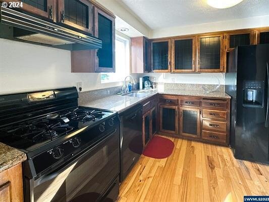 kitchen with black fridge with ice dispenser, light hardwood / wood-style flooring, light stone countertops, and a textured ceiling