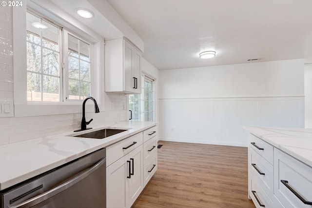 kitchen with white cabinetry, sink, stainless steel dishwasher, backsplash, and light hardwood / wood-style floors