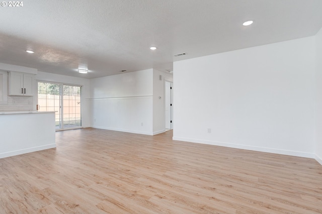 unfurnished living room with a textured ceiling and light hardwood / wood-style floors