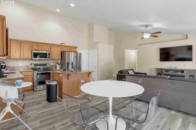 kitchen with appliances with stainless steel finishes, a breakfast bar area, a center island, light stone counters, and light hardwood / wood-style floors