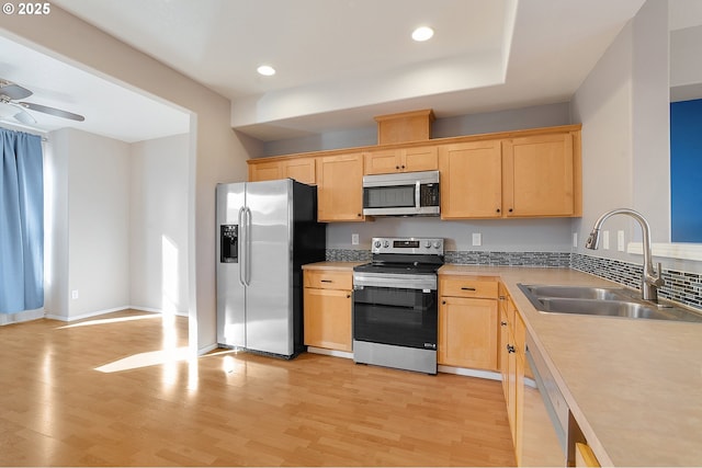 kitchen with appliances with stainless steel finishes, light brown cabinets, sink, light wood-type flooring, and ceiling fan