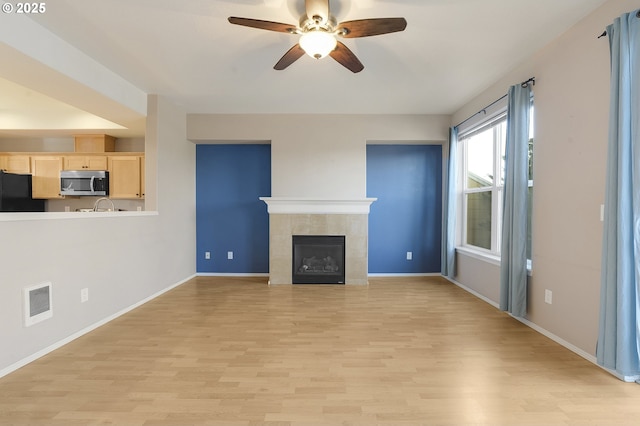 unfurnished living room featuring ceiling fan, a tile fireplace, and light hardwood / wood-style flooring