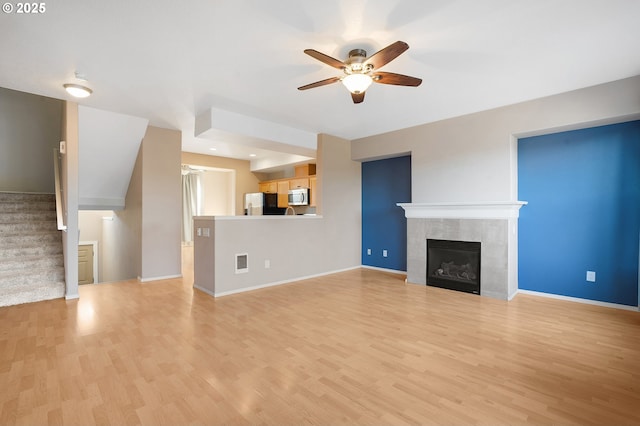 unfurnished living room with light wood-type flooring, ceiling fan, and a tiled fireplace