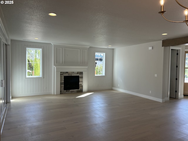 unfurnished living room featuring baseboards, a textured ceiling, light wood finished floors, recessed lighting, and a stone fireplace