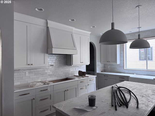 kitchen with wall chimney exhaust hood, black electric stovetop, decorative backsplash, decorative light fixtures, and a textured ceiling