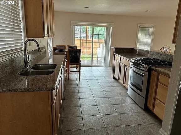 kitchen with light tile patterned floors, sink, dark stone counters, and stainless steel gas range