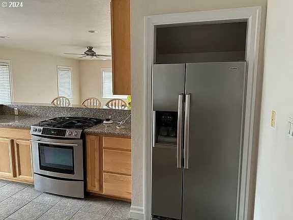 kitchen with a healthy amount of sunlight, appliances with stainless steel finishes, ceiling fan, and dark stone counters