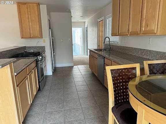 kitchen with dark stone countertops, dark tile patterned flooring, stainless steel appliances, and sink