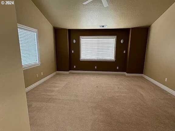 carpeted empty room featuring vaulted ceiling, ceiling fan, and a textured ceiling