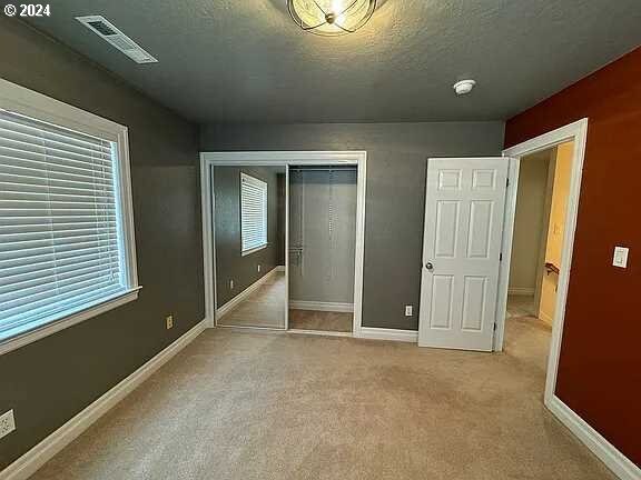 unfurnished bedroom featuring light colored carpet, a textured ceiling, and a closet