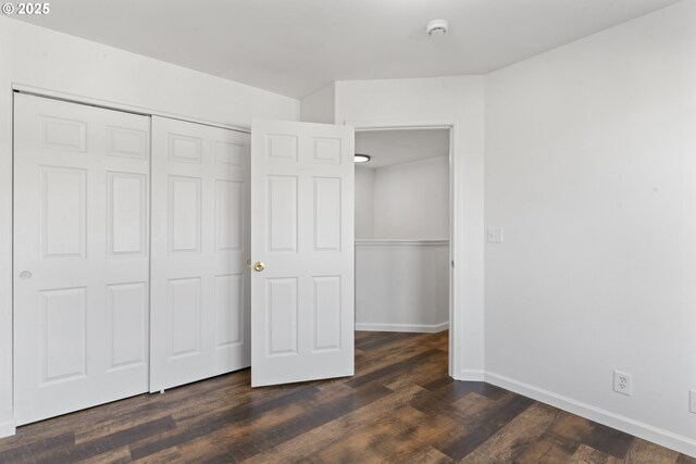 unfurnished bedroom with dark wood-style flooring, a closet, and baseboards