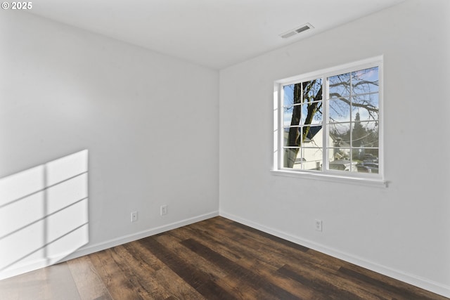 spare room with dark wood-style flooring, visible vents, and baseboards