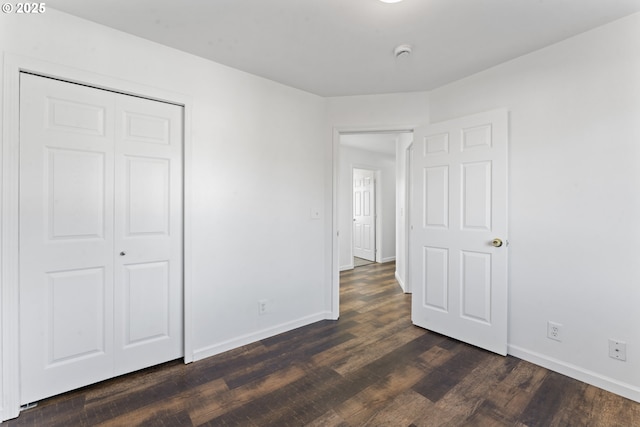 unfurnished bedroom featuring dark wood-style floors, baseboards, and a closet