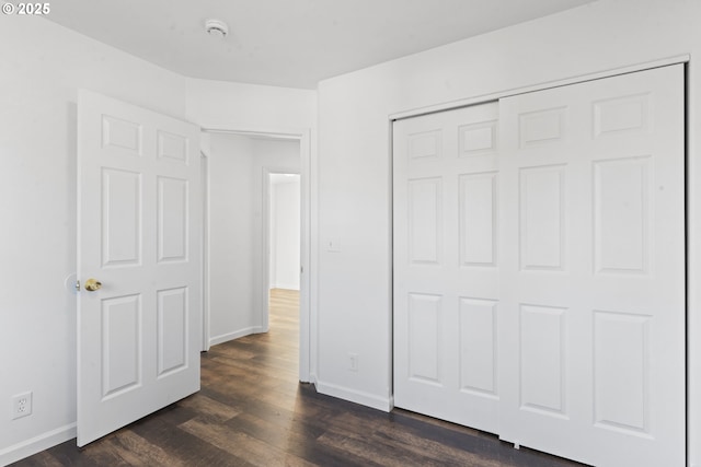 unfurnished bedroom featuring dark wood-style floors, a closet, and baseboards