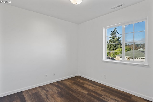 empty room featuring dark wood-style floors, visible vents, and baseboards