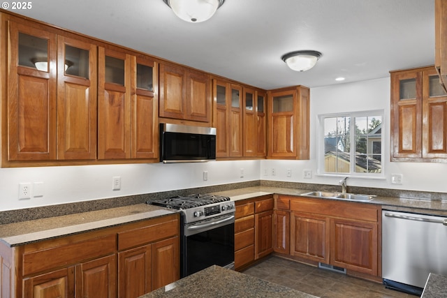 kitchen with visible vents, brown cabinetry, glass insert cabinets, appliances with stainless steel finishes, and a sink