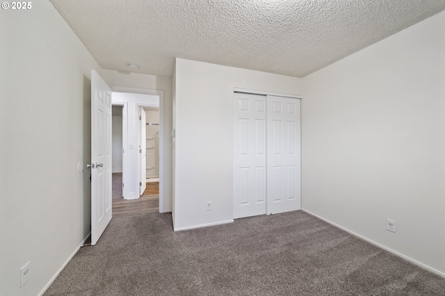 unfurnished bedroom featuring a textured ceiling, dark carpet, and a closet