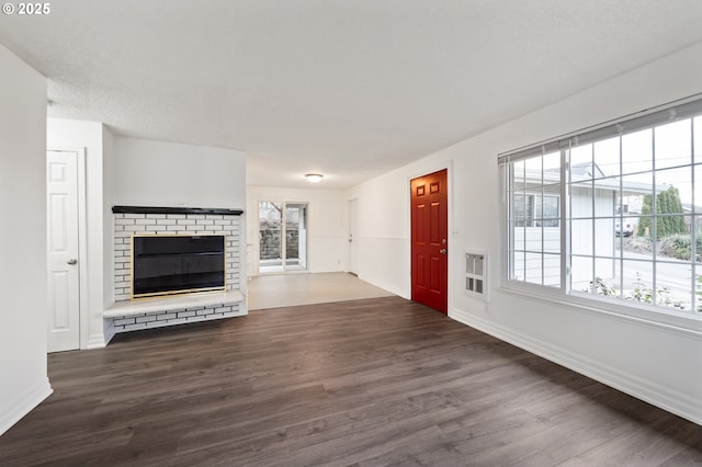 unfurnished living room featuring dark hardwood / wood-style flooring, a wealth of natural light, a fireplace, and heating unit