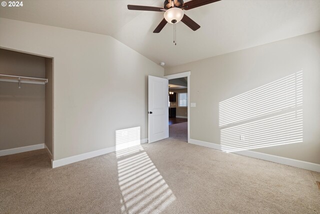 unfurnished bedroom featuring ceiling fan, light colored carpet, lofted ceiling, and a closet